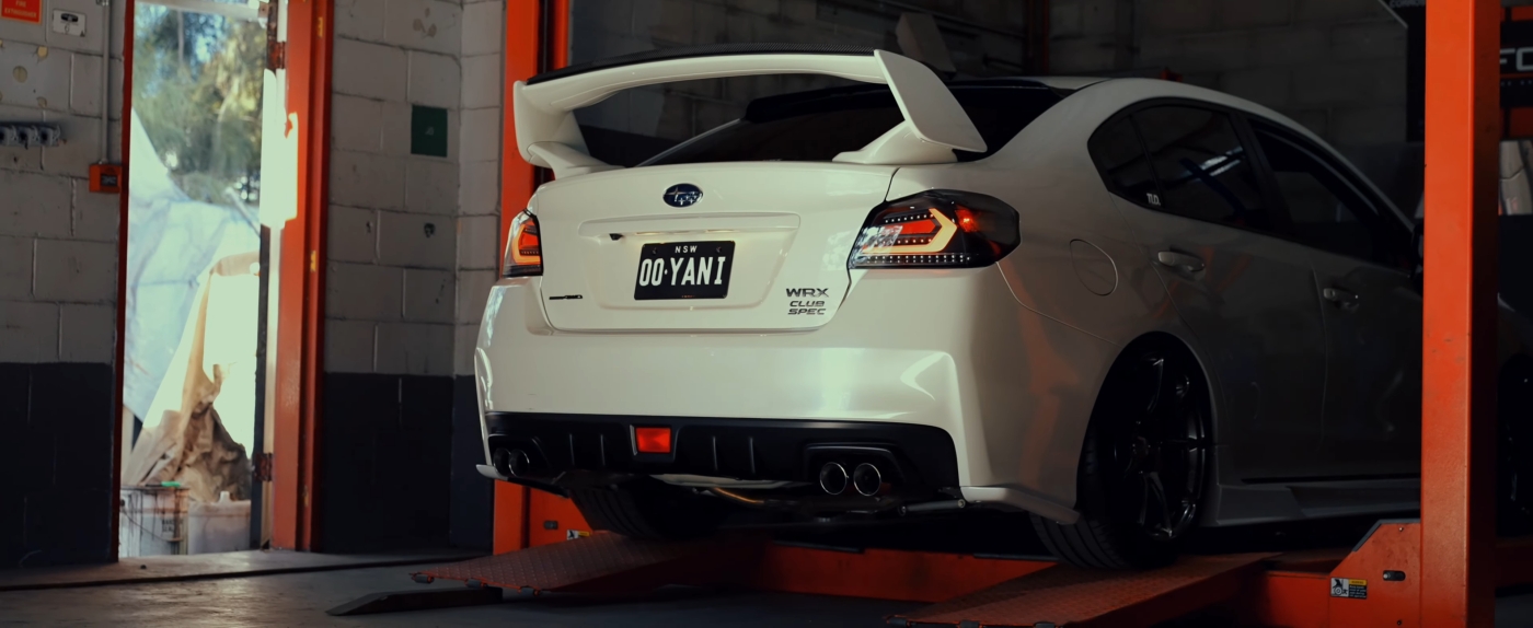 White Subaru WRX with XForce Exhaust System installed Club Spec on a vehicle lift in a garage.